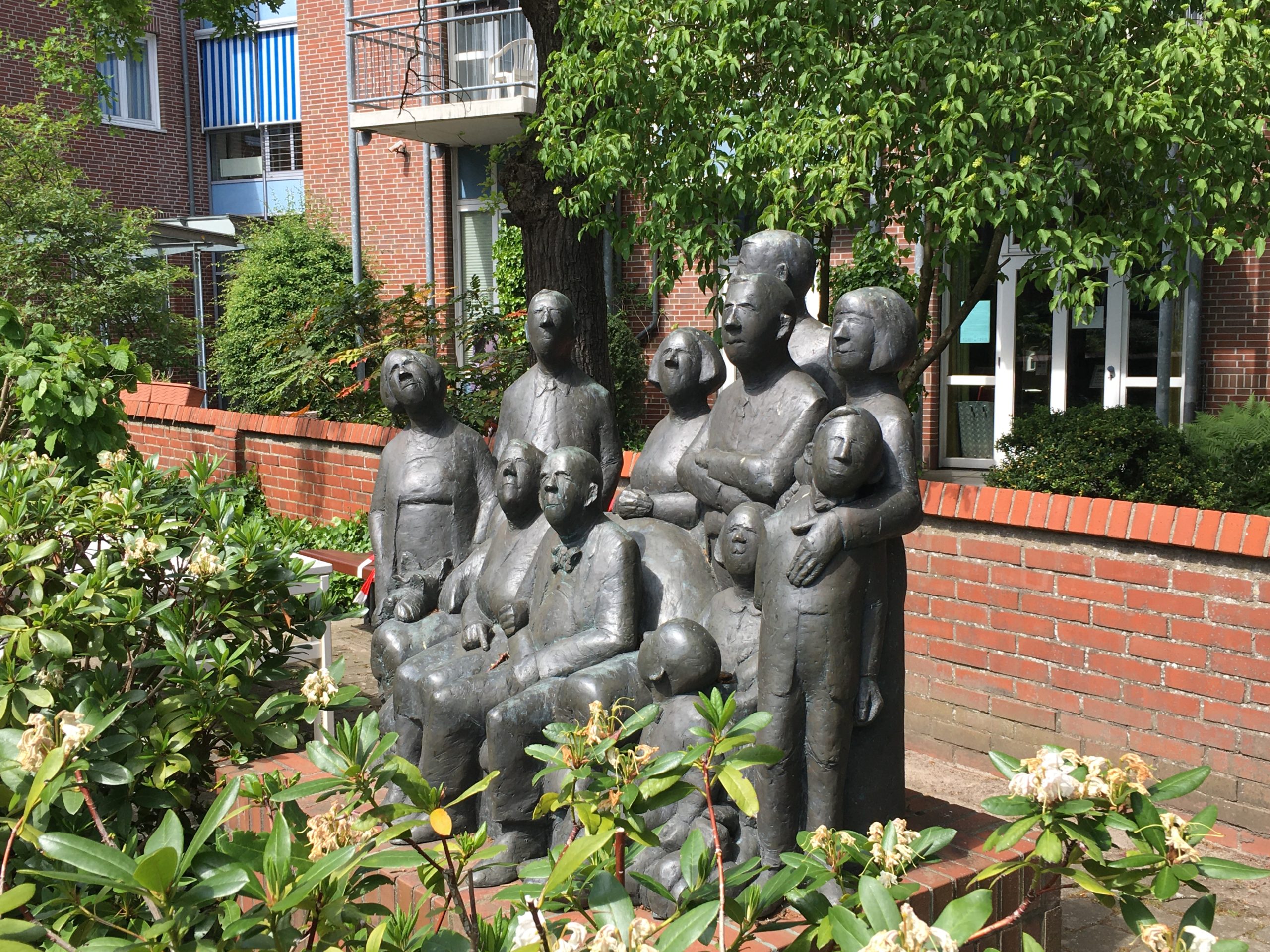 Skulpturen-Menschengruppe unterschiedlichen Alters sitzend und stehend vor dem Gebäude der Bremer Heimstiftung