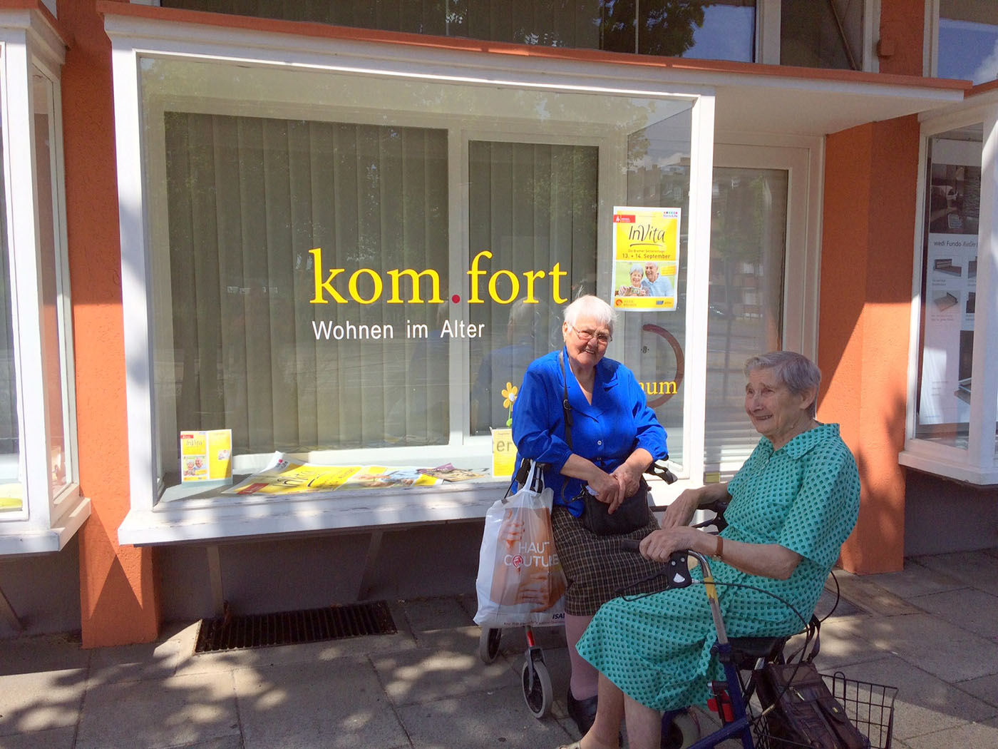 Zwei lächelnde, ältere Damen mit Rollator vor dem Schaufenster der Beratungsstelle