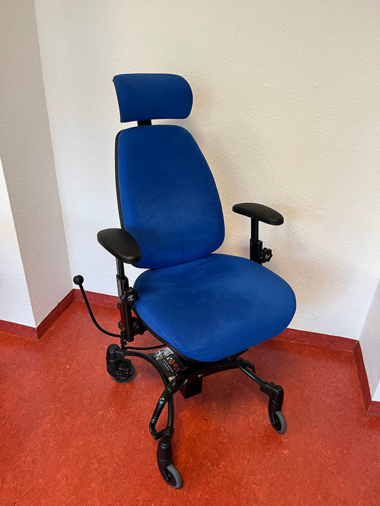 Vela-Stuhl: Rollender, höhenverstellbarer Stuhl mit Kopf- und Armlehnen, mit dem tiefliegende oder hochstehende Gegenstände erreicht werden können, z.B. Spülmaschine oder Teller im Hängeschrank.