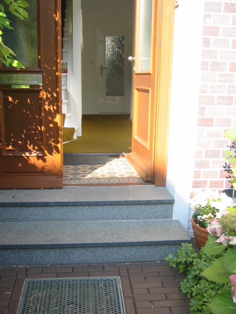 Eingang zu einem älteren Haus mit zwei Stufen, ohne Handlauf.