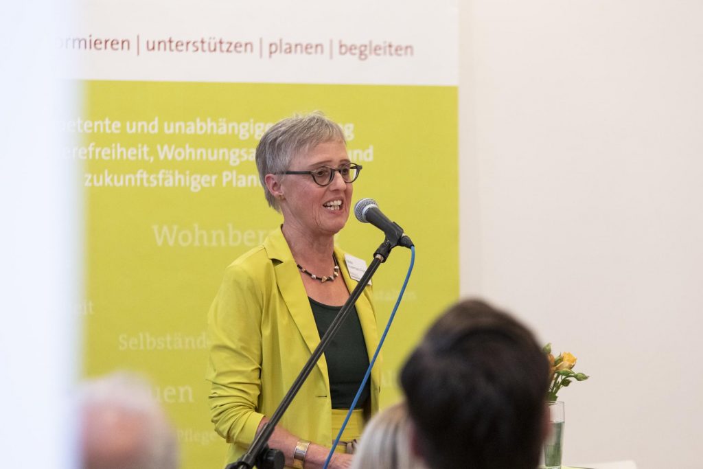 Meike Austermann-Frenz, im gelben Kostüm, vor dem Mikrofon bei ihrem Rückblick auf 20 Jahre Beratungsarbeit