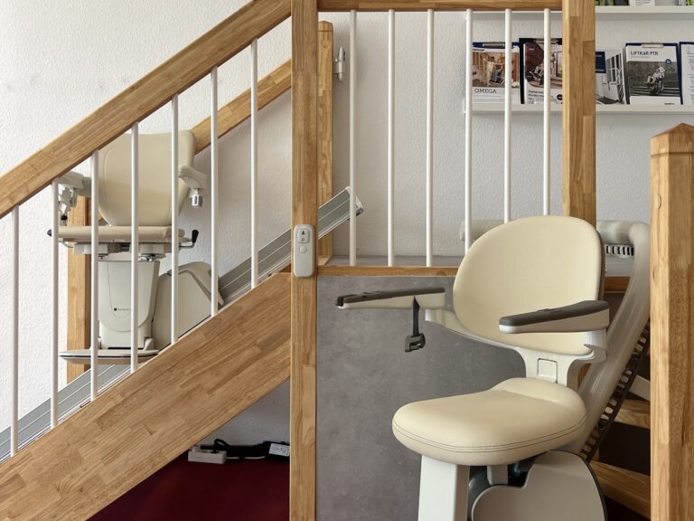 Zwei Treppenlifte an einem Holzpodest. Einer an einer kurvigen Treppe und einer an einer geraden Treppe.